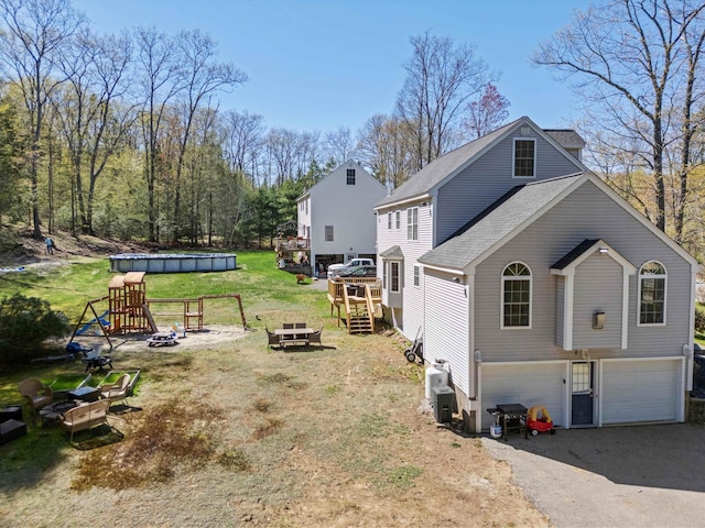 view of side of home with a fire pit, a lawn, a shingled roof, an attached garage, and driveway