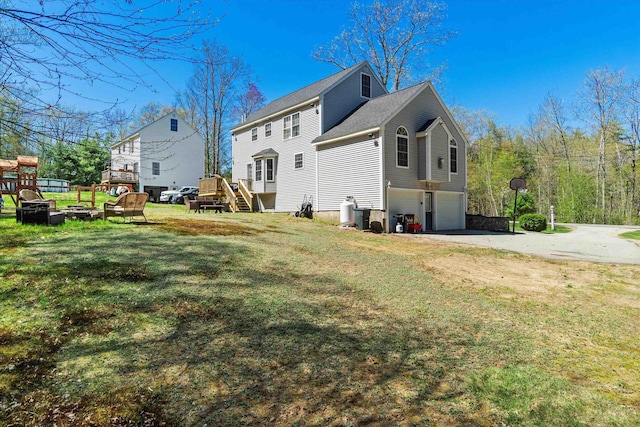 rear view of property featuring a wooden deck, aphalt driveway, a yard, an attached garage, and stairs