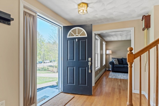 foyer entrance with stairs, baseboards, a baseboard radiator, and light wood-type flooring