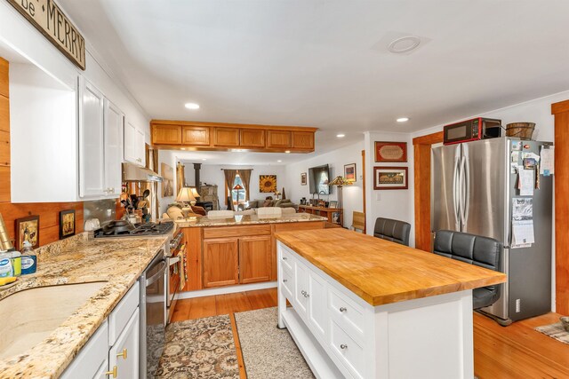 kitchen with appliances with stainless steel finishes, butcher block counters, open floor plan, recessed lighting, and light wood-style flooring