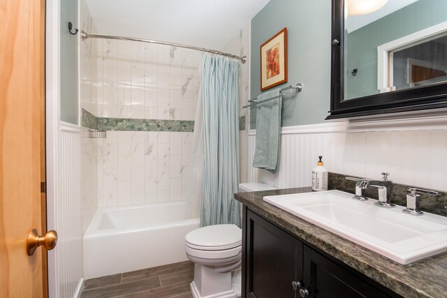 full bathroom featuring vanity, wainscoting, wood finished floors, toilet, and shower / bathtub combination with curtain