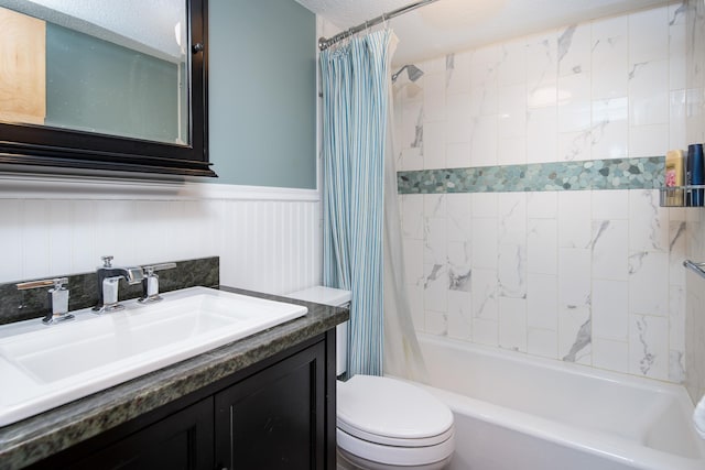 full bath with vanity, wainscoting, toilet, a textured ceiling, and shower / bath combo