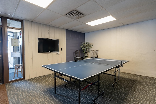 recreation room featuring carpet floors, wooden walls, a drop ceiling, and visible vents