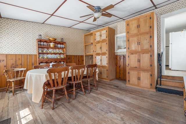 dining space featuring wallpapered walls, wainscoting, ceiling fan, and hardwood / wood-style floors