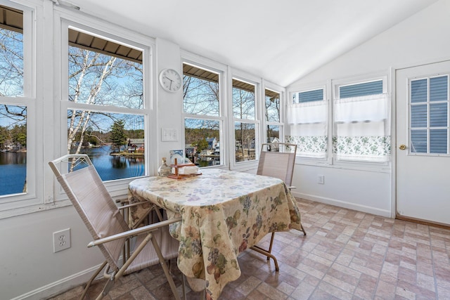 sunroom with a water view, baseboards, brick floor, and lofted ceiling