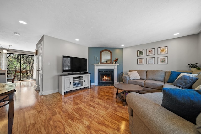 living area with recessed lighting, a warm lit fireplace, baseboards, and light wood-style floors