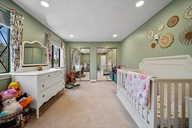 bedroom featuring multiple windows, light carpet, two closets, and recessed lighting