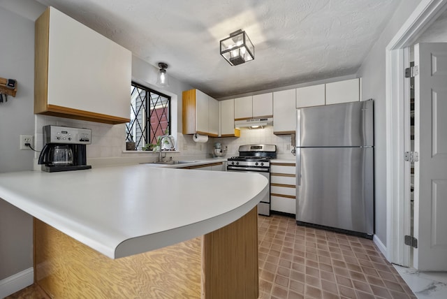 kitchen featuring a peninsula, light countertops, under cabinet range hood, a sink, and appliances with stainless steel finishes