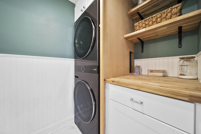 washroom with stacked washer and dryer, baseboards, wainscoting, and marble finish floor