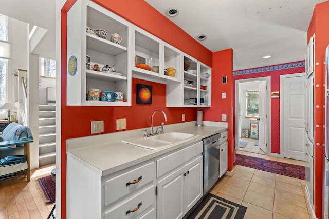 kitchen featuring stainless steel dishwasher, open shelves, light countertops, white cabinets, and a sink