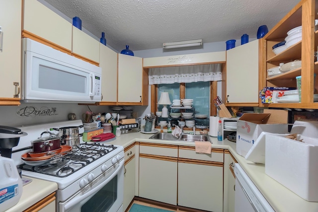kitchen featuring light countertops, a sink, a textured ceiling, and white appliances