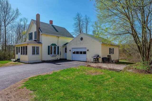 view of home's exterior with a garage, a chimney, a yard, and driveway