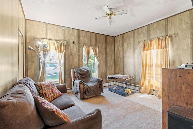 sitting room with carpet floors, wooden walls, baseboard heating, a textured ceiling, and a ceiling fan
