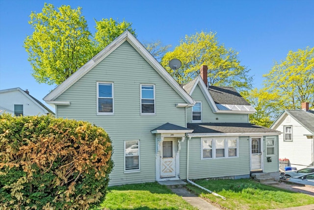 view of front of property with entry steps, a chimney, a shingled roof, and a front yard