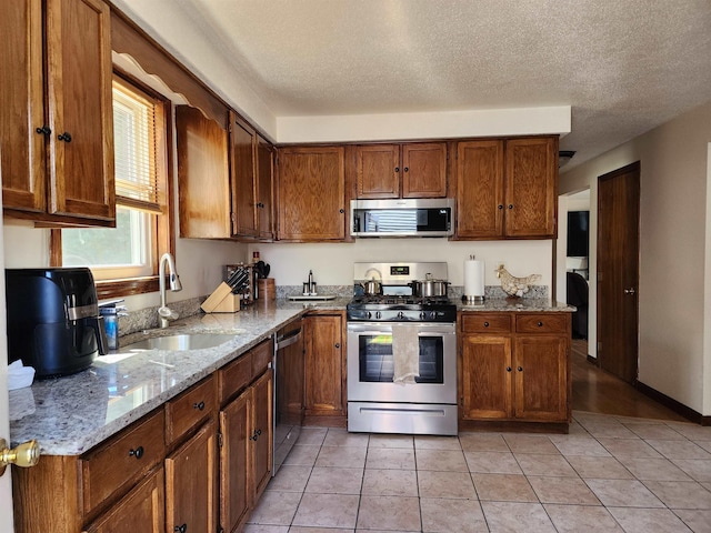 kitchen featuring light stone counters, a sink, brown cabinets, and stainless steel appliances