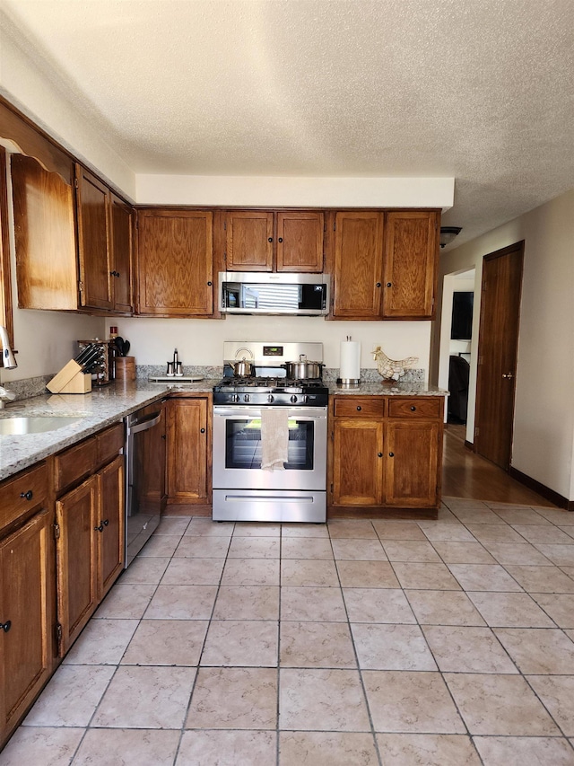 kitchen featuring a sink, appliances with stainless steel finishes, brown cabinetry, and a textured ceiling
