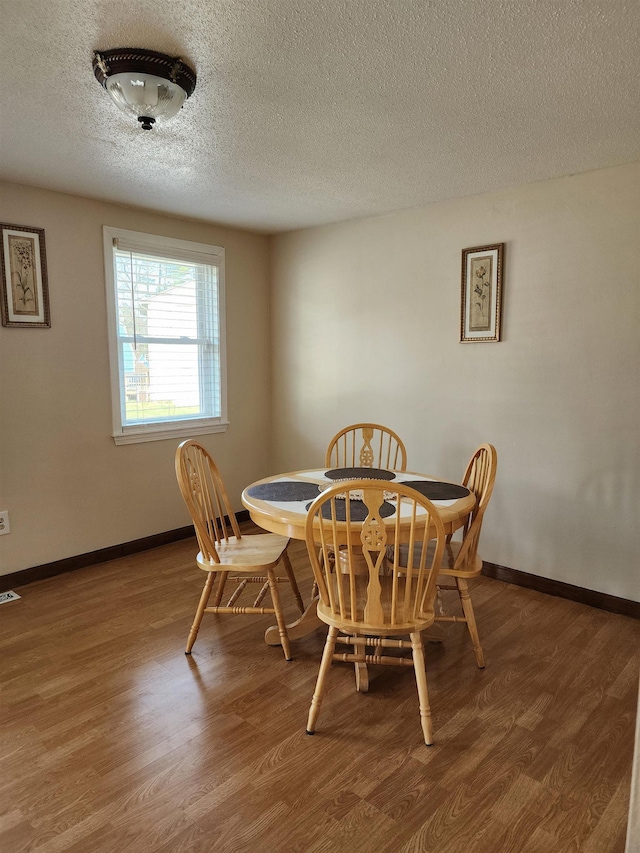 dining area featuring baseboards, a textured ceiling, visible vents, and wood finished floors