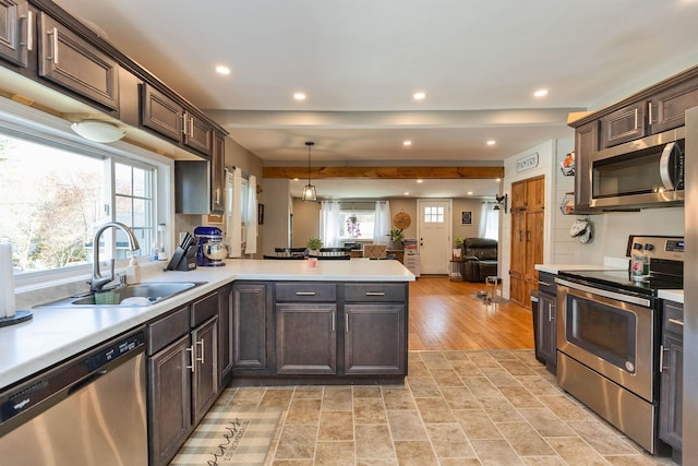 kitchen with a peninsula, dark brown cabinetry, light countertops, a sink, and appliances with stainless steel finishes