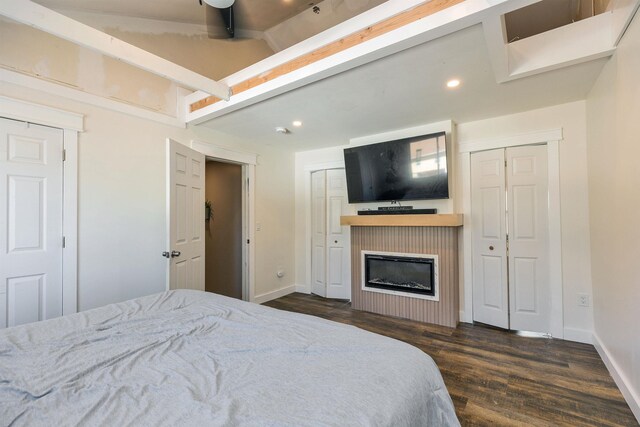 bedroom featuring a glass covered fireplace, two closets, baseboards, dark wood-style floors, and recessed lighting
