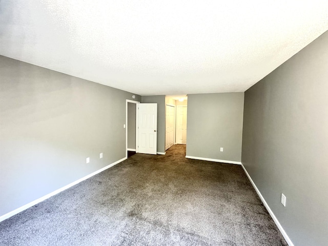 spare room featuring a textured ceiling, baseboards, and dark carpet