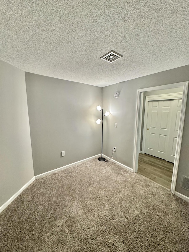 empty room featuring visible vents, carpet flooring, a textured ceiling, and baseboards