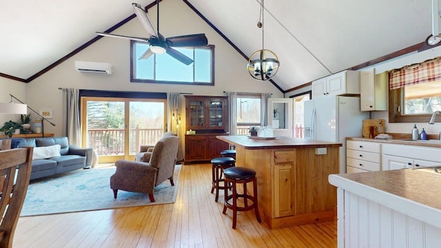 kitchen featuring ceiling fan, high vaulted ceiling, an AC wall unit, light wood-type flooring, and a sink