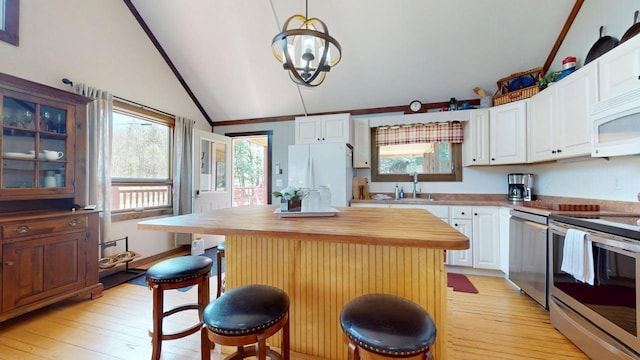 kitchen featuring white cabinetry, a sink, light wood finished floors, vaulted ceiling, and stainless steel appliances