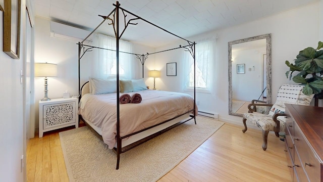 bedroom with a wall mounted air conditioner, a baseboard heating unit, and light wood-style flooring