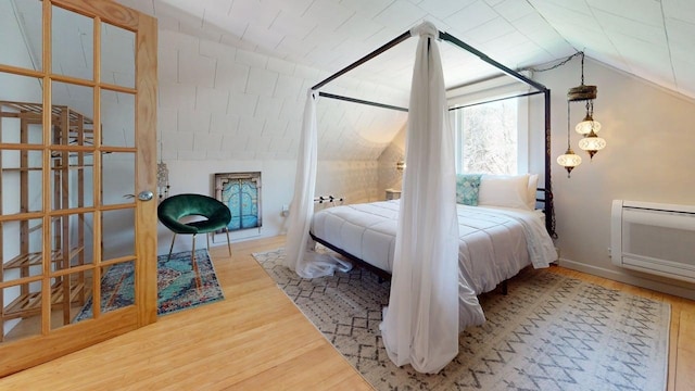 bedroom featuring a wall unit AC, vaulted ceiling, and wood finished floors