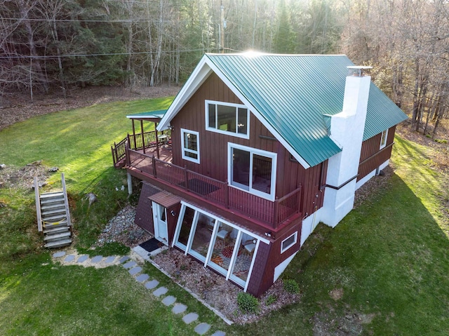 exterior space with a wooden deck, a chimney, stairs, a yard, and a forest view