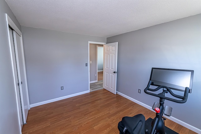 exercise area with baseboards, a textured ceiling, and wood finished floors