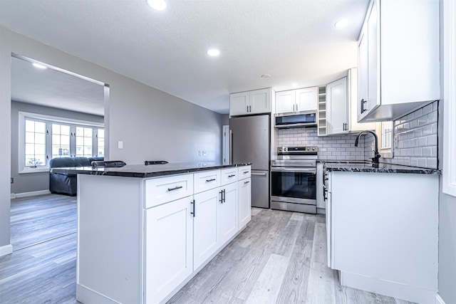 kitchen with a kitchen island, backsplash, light wood finished floors, stainless steel appliances, and white cabinetry