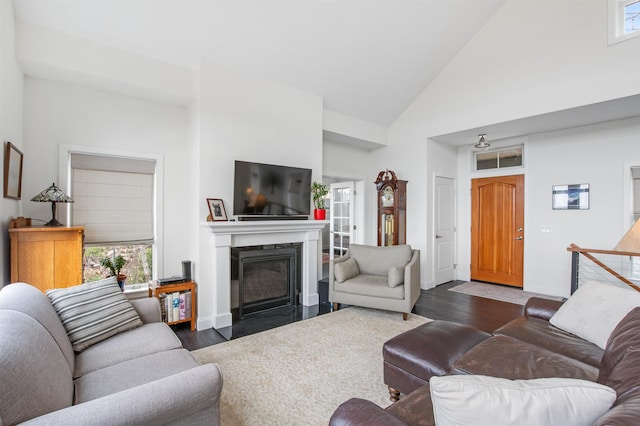 living area with dark wood-style flooring, high vaulted ceiling, a glass covered fireplace, and baseboards