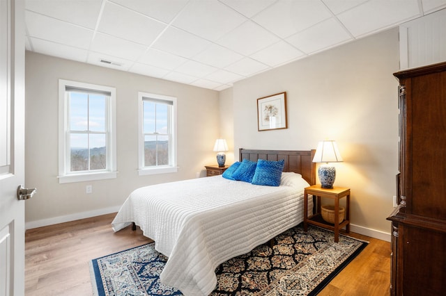 bedroom featuring baseboards, a drop ceiling, wood finished floors, and visible vents