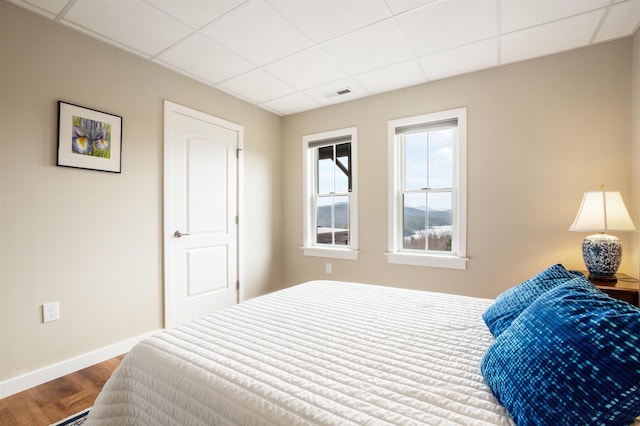 bedroom with dark wood-type flooring, a paneled ceiling, baseboards, and visible vents