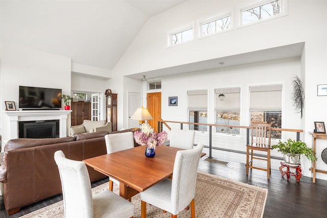 dining space featuring a fireplace, wood finished floors, and high vaulted ceiling