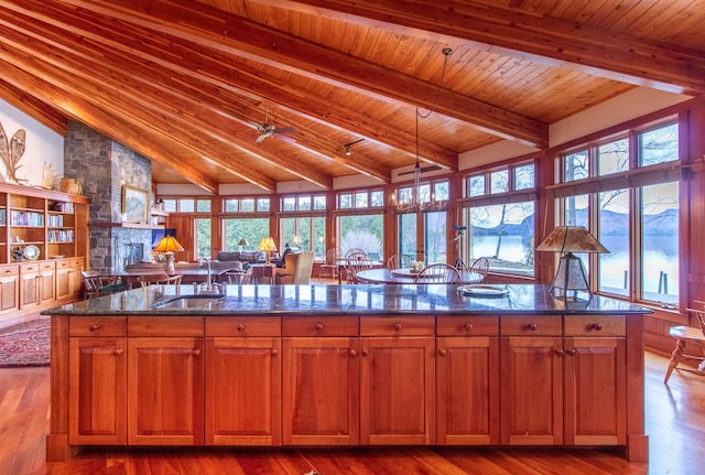 kitchen with wood ceiling, a center island with sink, a sink, dark stone counters, and vaulted ceiling with beams