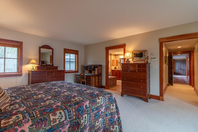 bedroom featuring baseboards, connected bathroom, and light carpet