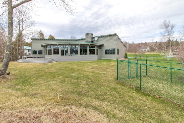 rear view of house featuring a sunroom, a lawn, fence, and a chimney