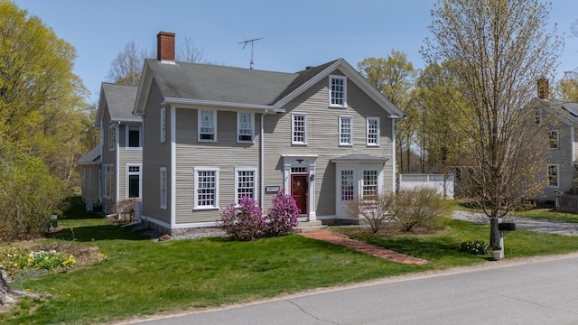 colonial-style house featuring a chimney and a front lawn