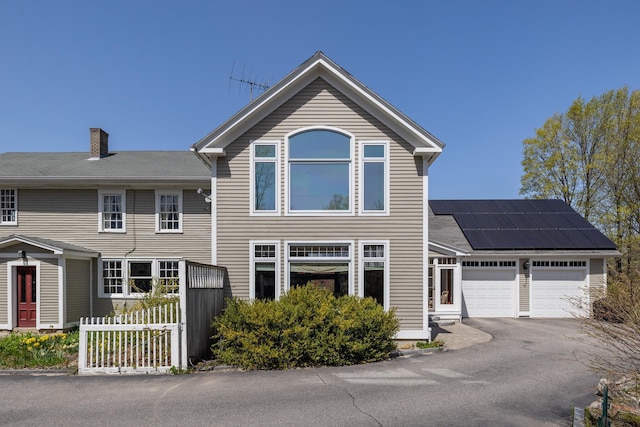 view of front facade with fence, a garage, a chimney, solar panels, and driveway