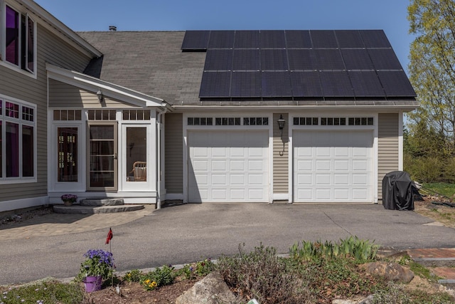 exterior space with a garage, aphalt driveway, roof mounted solar panels, and roof with shingles