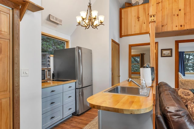 kitchen with a sink, stainless steel appliances, butcher block countertops, and a notable chandelier