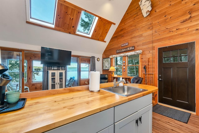 kitchen with wood finished floors, a sink, high vaulted ceiling, wooden walls, and butcher block countertops