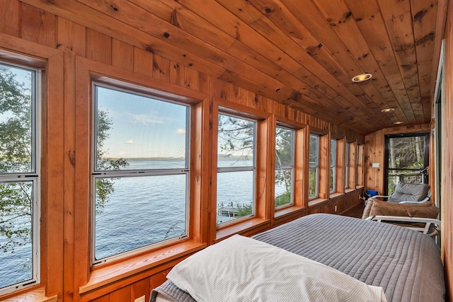 bedroom featuring a water view, multiple windows, and wood walls