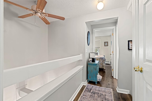 corridor with a textured ceiling, dark wood finished floors, and baseboards