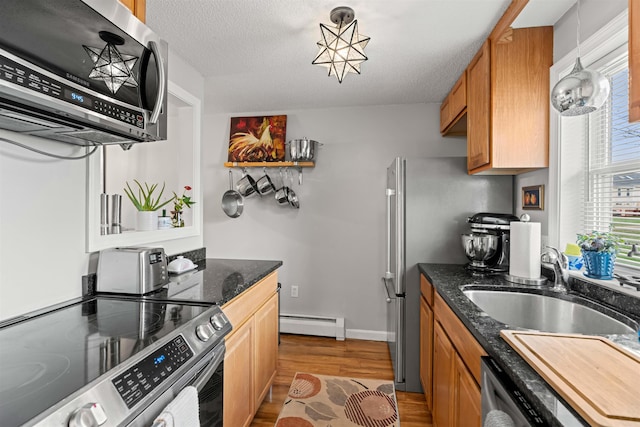 kitchen with appliances with stainless steel finishes, a sink, light wood-style floors, dark stone countertops, and a baseboard heating unit
