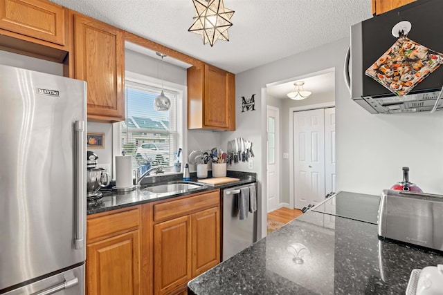 kitchen featuring brown cabinetry, light wood-type flooring, dark stone counters, a sink, and stainless steel appliances