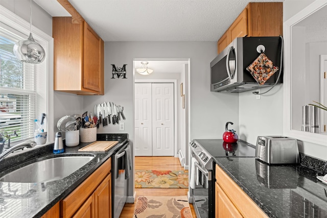 kitchen featuring brown cabinets, stainless steel appliances, a sink, and dark stone countertops