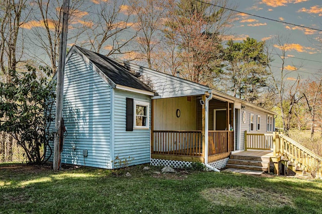 view of front of home with a lawn, covered porch, and a shingled roof